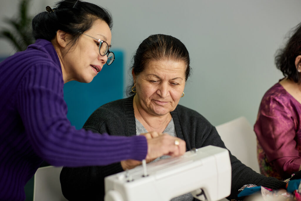 A Fair Foundations staff member supports a participant in the sewing and crafts group as they work together on a sewing machine.