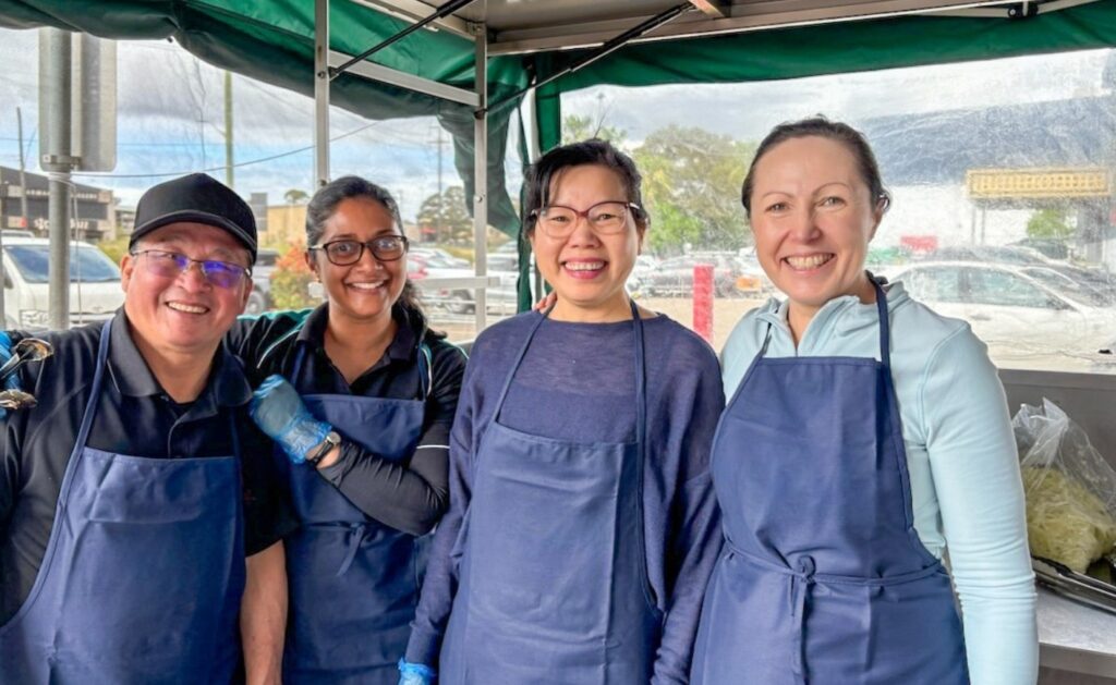 Group of 4 staff and volunteers hosting a fundraising BBQ, looking at the camera, smiling.